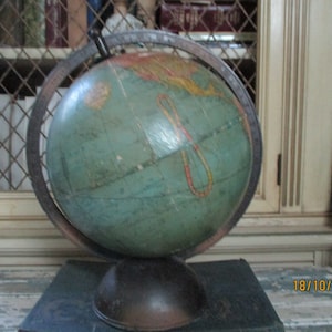 Może przedstawiać: Antyczny globus z zieloną i niebieską mapą na metalowej podstawie. Globus stoi na ciemnej powierzchni z datą stempla w prawym dolnym rogu.