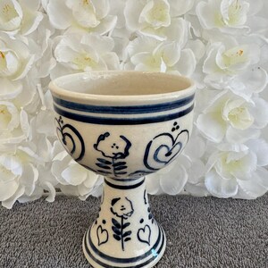 May include: A white ceramic goblet with a blue floral design. The goblet has a wide bowl and a tall, slender stem.