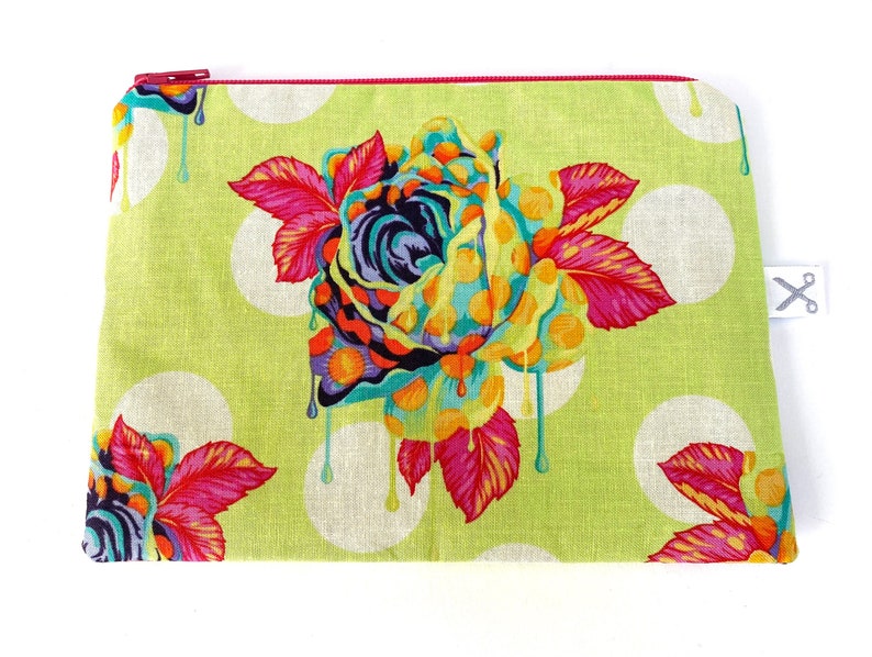May include: A green zippered pouch with a white polka dot pattern and a colorful dripping rose design. The rose is made up of pink, yellow, blue, and green colors.