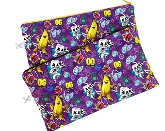 Könnte beinhalten: Zwei lila Reißverschlusstaschen mit einem sich wiederholenden Muster aus Cartoon-Bananen, Marshmallow-Charakteren und Blitzen. Die Taschen haben goldene Reißverschlüsse und das Wort "OG" ist im gesamten Design aufgedruckt. Die Taschen dienen wahrscheinlich zur Aufbewahrung kleiner Gegenstände.