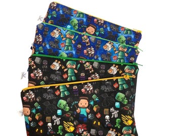 Könnte beinhalten: Vier Reißverschlusstaschen mit einem Minecraft-Themenmuster. Die Taschen zeigen ein sich wiederholendes Design von Minecraft-Charakteren und -Elementen auf einem schwarzen, blauen und grünen Hintergrund. Jede Tasche hat einen unterschiedlich farbigen Reißverschluss: gelb, grün und blau.