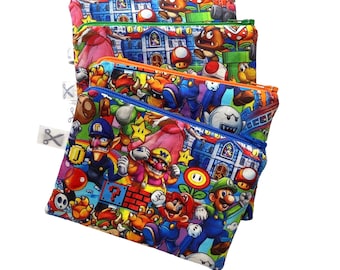 Könnte beinhalten: Drei Reißverschlusstaschen mit farbenfrohen Super Mario Bros. Charakterdesigns. Die Taschen zeigen Mario, Luigi und Bowser vor dem Hintergrund von Burgen und Spielelementen. Jede Tasche hat einen Reißverschluss in einer anderen Farbe.