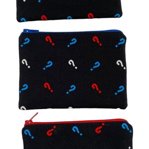 Puede incluir: Tres bolsas negras con cremallera con un patr&oacute;n repetitivo de signos de interrogaci&oacute;n blancos, azules y rojos.