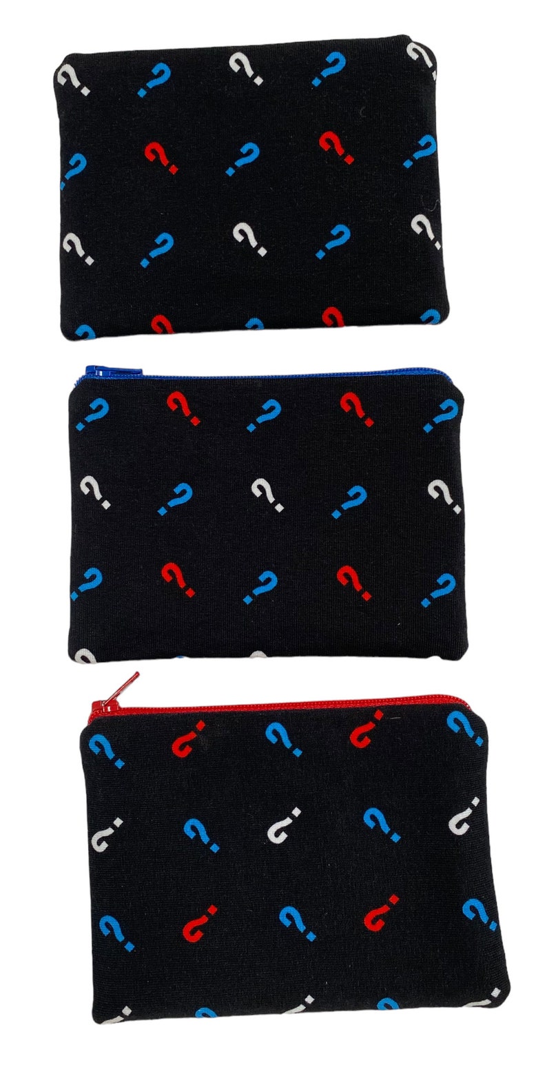 Puede incluir: Tres bolsas negras con cremallera con un patr&oacute;n repetitivo de signos de interrogaci&oacute;n blancos, azules y rojos.