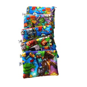 Puede incluir: Una pila de seis bolsas con cremallera de colores con un estampado de personajes de Minecraft. Las bolsas están hechas de tela y tienen un fondo azul con varios personajes de Minecraft, incluidos Steve, un creeper y un cerdo.
