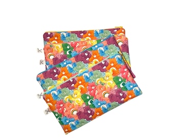 Könnte beinhalten: Drei farbenfrohe Reißverschlusstaschen mit einem sich wiederholenden Muster von Cartoon-Bären in verschiedenen Farben. Die Taschen haben eine gesteppte Textur und einen Reißverschluss. Der Hintergrund ist weiß.