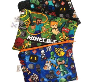 Könnte beinhalten: Drei Reißverschlusstaschen mit Minecraft-Motiven. Die obere Tasche ist schwarz mit Minecraft-Charakteren. Die mittlere Tasche ist grün mit dem Wort "Minecraft". Die untere Tasche ist blau mit Minecraft-Charakteren. Jede Tasche hat einen Reißverschluss.