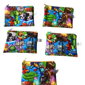 May include: Set of five colorful zippered pouches featuring a Minecraft theme. The pouches are made of fabric and have a variety of Minecraft characters and items printed on them, including Steve, Creeper, and a horse.