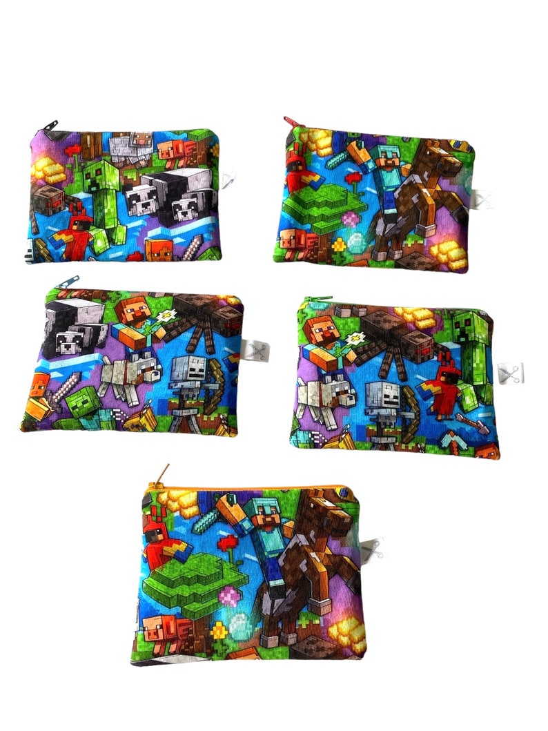 May include: Set of five colorful zippered pouches featuring a Minecraft theme. The pouches are made of fabric and have a variety of Minecraft characters and items printed on them, including Steve, Creeper, and a horse.
