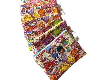 May include: A stack of eight colorful zippered pouches with a retro cartoon print of girls with rainbow hair and stars.
