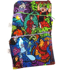 Puede incluir: Una colorida bolsa con cremallera con ilustraciones de personajes animados al estilo vidriera. La bolsa tiene un fondo negro con imágenes de villanos y héroes en colores vibrantes. La bolsa tiene tres compartimentos con cremallera con cremalleras moradas, verdes y rojas.