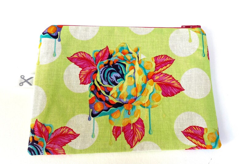 May include: A green zippered pouch with a white polka dot pattern and a colorful dripping rose design.