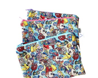 Könnte beinhalten: Drei Reißverschlusstaschen mit blauem Hintergrund und einem bunten Muster von Disney-Charakteren, darunter Mickey Mouse, Minnie Mouse, Donald Duck und Alice im Wunderland. Die Taschen sind übereinander gestapelt.