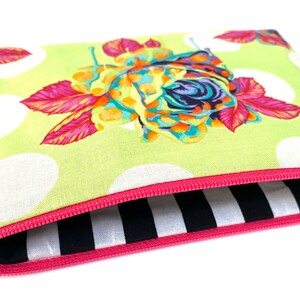 May include: A green zippered pouch with a white polka dot pattern and a colorful floral design. The pouch is lined with black and white stripes.