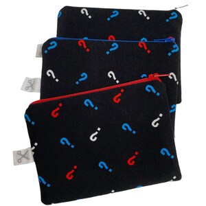 Puede incluir: Tres bolsas negras con cremallera con un patr&oacute;n de signos de interrogaci&oacute;n. Las bolsas est&aacute;n apiladas una encima de la otra. La bolsa superior tiene una cremallera azul, la bolsa del medio tiene una cremallera roja y la bolsa inferior tiene una cremallera blanca.