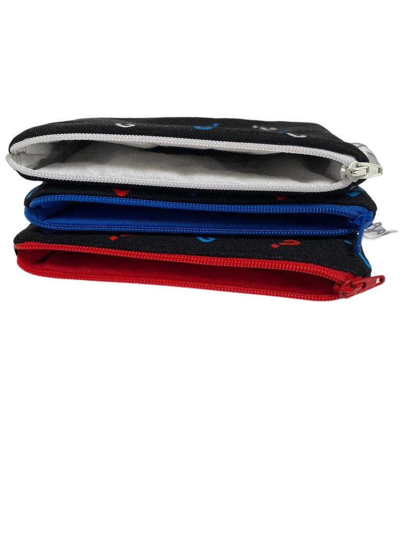Puede incluir: Cuatro bolsas negras con cremallera y forros de diferentes colores. Las bolsas est&aacute;n apiladas una encima de la otra. La bolsa superior tiene un forro blanco, la segunda bolsa tiene un forro azul, la tercera bolsa tiene un forro rojo y la bolsa inferior tiene un forro negro.