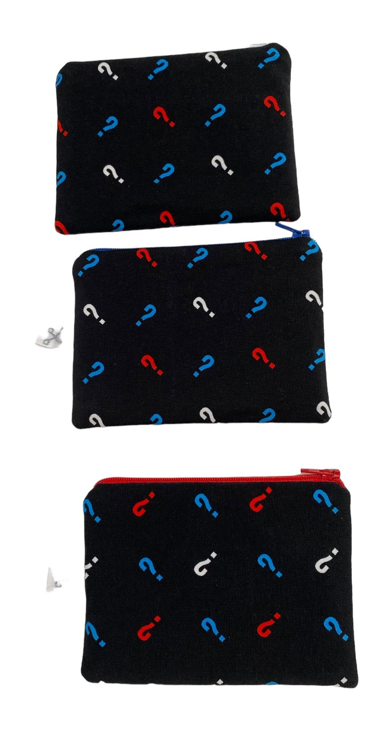 Puede incluir: Tres bolsas negras con cremallera con un patr&oacute;n repetido de signos de interrogaci&oacute;n rojos, azules y blancos.