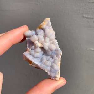 May include: A blue and white agate geode with a cluster of small, round, white crystals. The geode is a natural formation and has a rough, irregular shape.