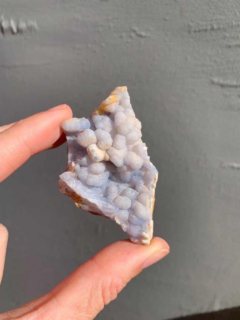 May include: A blue and white agate geode with a cluster of small, round, white crystals. The geode is a natural formation and has a rough, irregular shape.
