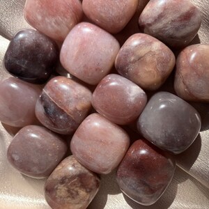 May include: A collection of tumbled stones with a mix of pink, brown, and white colors. The stones are smooth and polished, with a variety of patterns and textures.