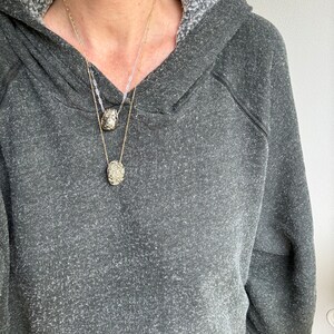 May include: A person wearing a gray hooded sweatshirt with two gold necklaces featuring textured oval pendants.
