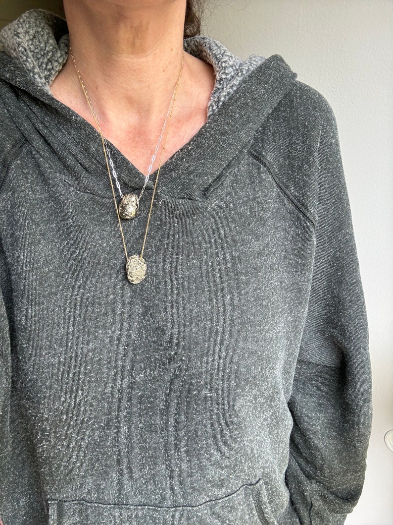 May include: A person wearing a gray hooded sweatshirt with two gold necklaces featuring textured oval pendants.