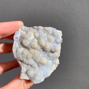 May include: A light blue and white agate geode with a rough, textured surface. The geode has a cluster of small, round crystals.