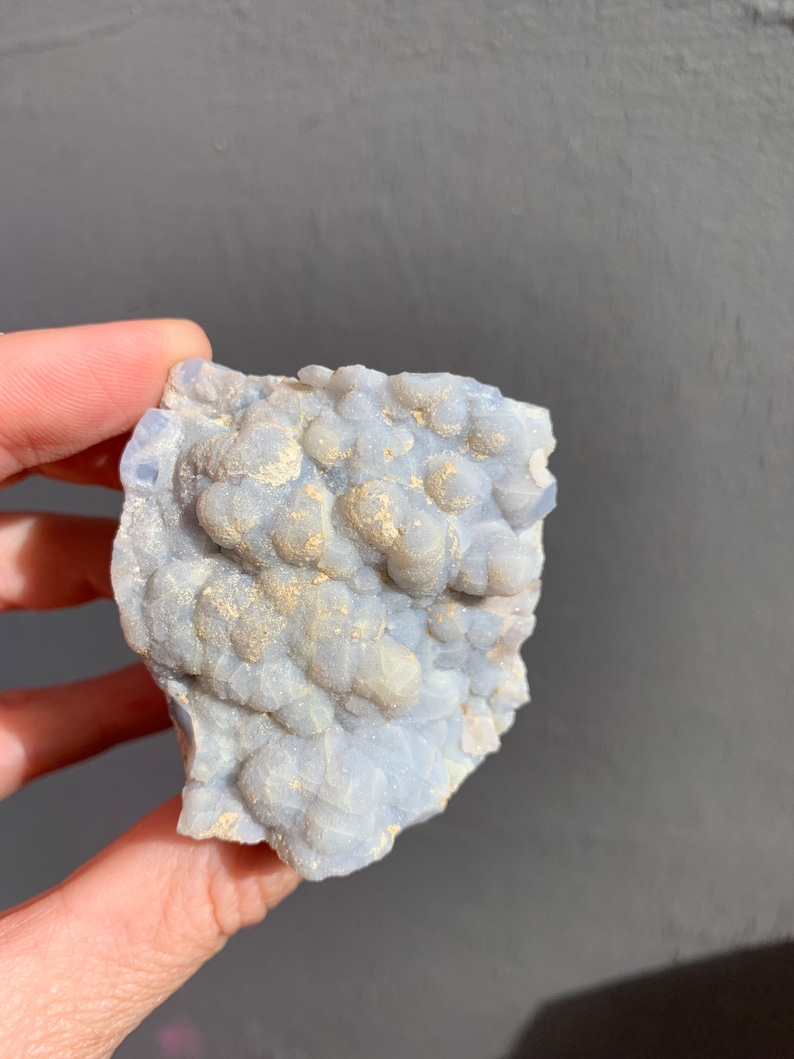 May include: A light blue and white agate geode with a rough, textured surface. The geode has a cluster of small, round crystals.