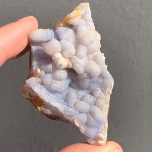 May include: A blue and white agate geode with a cluster of small, round nodules. The geode is a natural formation and has a rough, irregular shape.