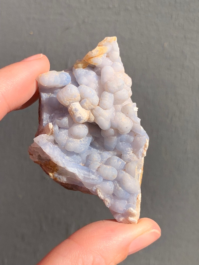 May include: A blue and white agate geode with a cluster of small, round nodules. The geode is a natural formation and has a rough, irregular shape.