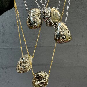 May include: Five gold and silver chains with large, irregular, pyrite stone pendants. The stones are a dark, metallic silver color with a rough, textured surface.