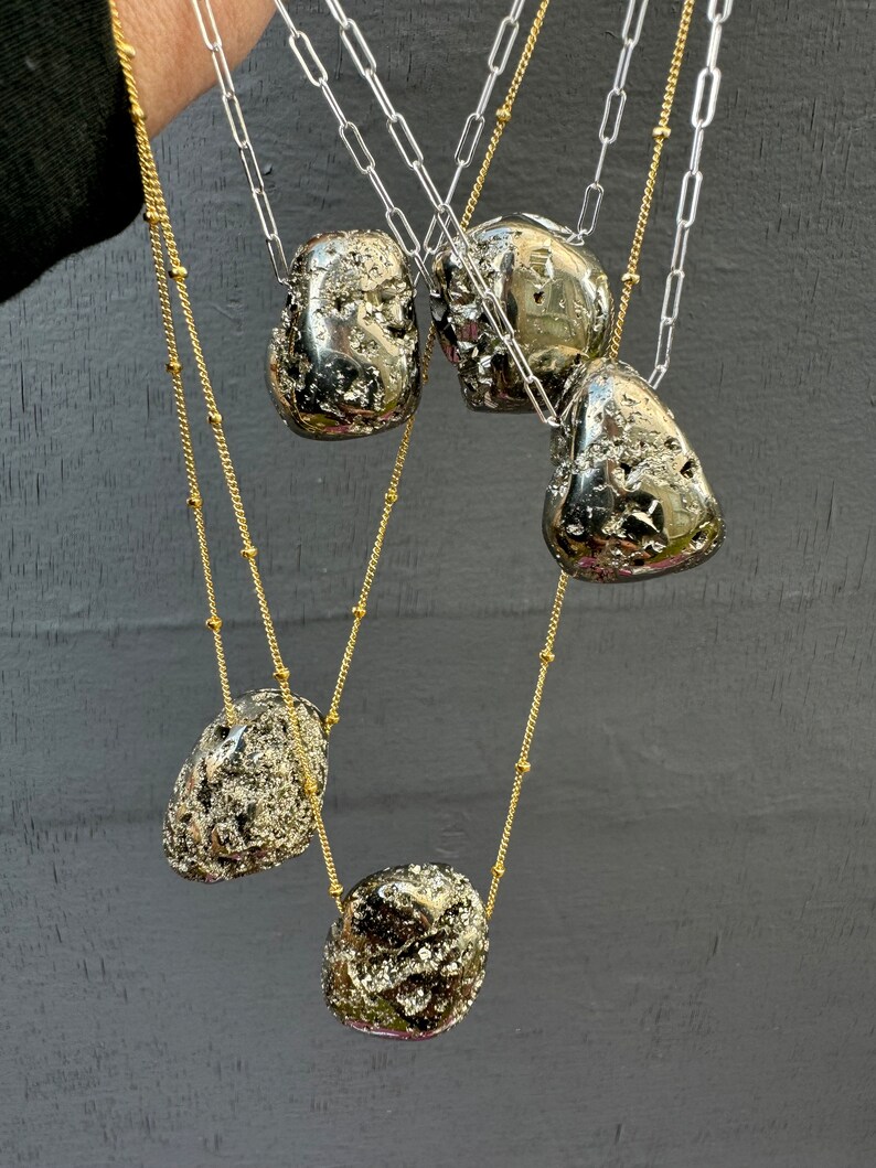 May include: Five gold and silver chains with large, irregular, pyrite stone pendants. The stones are a dark, metallic silver color with a rough, textured surface.