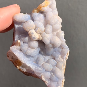 May include: A blue and white agate geode with a cluster of small, round nodules. The geode has a rough, natural texture and is a beautiful example of this type of crystal.
