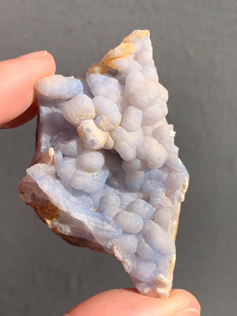 May include: A blue and white agate geode with a cluster of small, round nodules. The geode has a rough, natural texture and is a beautiful example of this type of crystal.