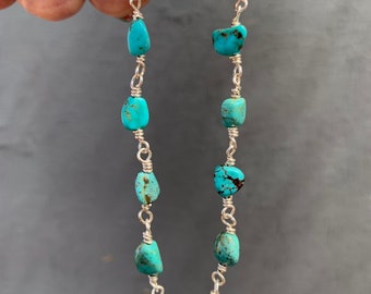 May include: A turquoise gemstone bracelet. The bracelet features irregular, light blue-green turquoise stones strung together with silver-colored wire. The stones vary in size and shape, creating a unique, handcrafted look. The bracelet is held against a gray background.