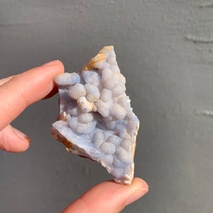 May include: A blue and white agate geode with a cluster of small, round nodules. The geode is irregularly shaped and has a rough, natural surface.