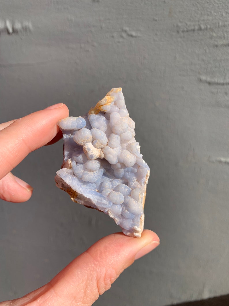 May include: A blue and white agate geode with a cluster of small, round nodules. The geode is irregularly shaped and has a rough, natural surface.