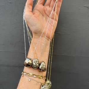 May include: Five gold and silver necklaces with pyrite stone pendants. The necklaces are layered and feature different chain styles.