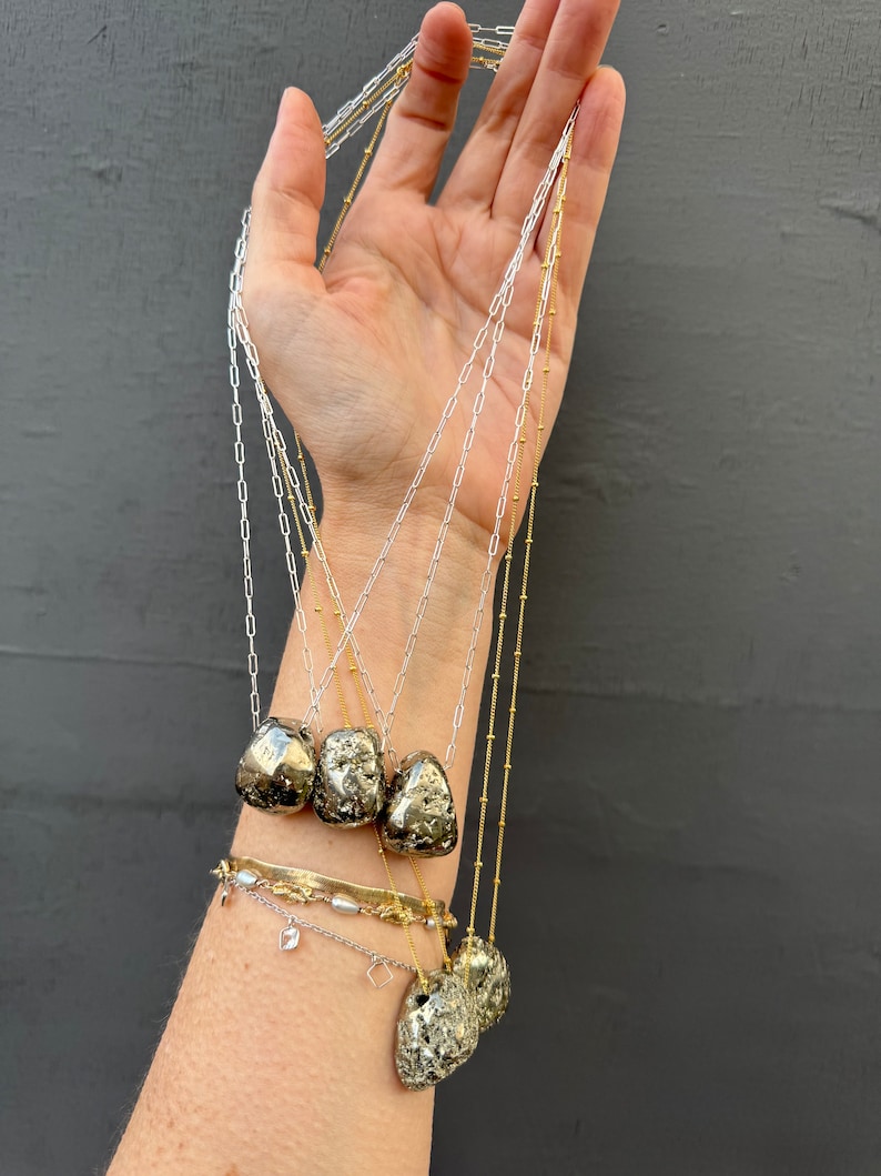 May include: Five gold and silver necklaces with pyrite stone pendants. The necklaces are layered and feature different chain styles.