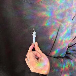 Pu&ograve; includere: Un ciondolo d'argento con un cristallo trasparente e un design dettagliato. Il ciondolo &egrave; tenuto da una mano.