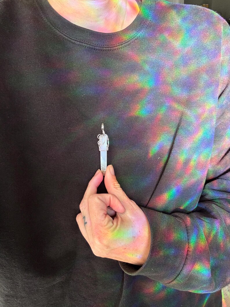 Pu&ograve; includere: Un ciondolo d'argento con un cristallo trasparente e un design dettagliato. Il ciondolo &egrave; tenuto da una mano.