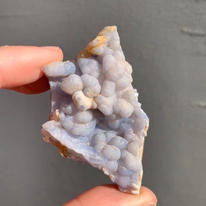 May include: A blue and white agate geode with a cluster of small, round, white crystals. The geode is a natural formation and has a rough, irregular shape.