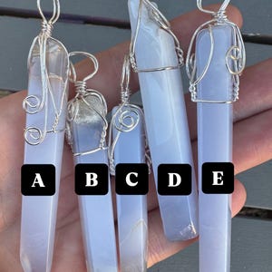 Pu&ograve; includere: Cinque ciondoli in cristallo di agata blu avvolti in filo d'argento. I ciondoli sono etichettati dalla A alla E.