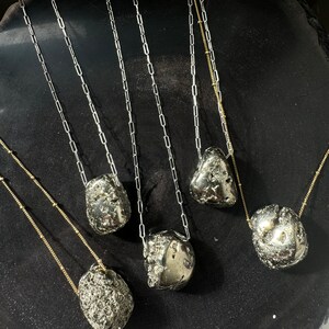 May include: Five necklaces with different length chains and pyrite stone pendants. The chains are silver and gold in color. The stones are a dark gray with a metallic sheen.