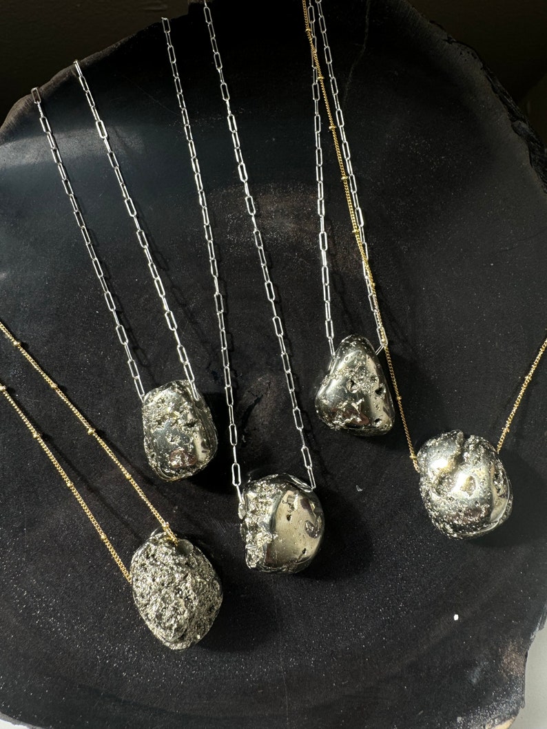 May include: Five necklaces with different length chains and pyrite stone pendants. The chains are silver and gold in color. The stones are a dark gray with a metallic sheen.