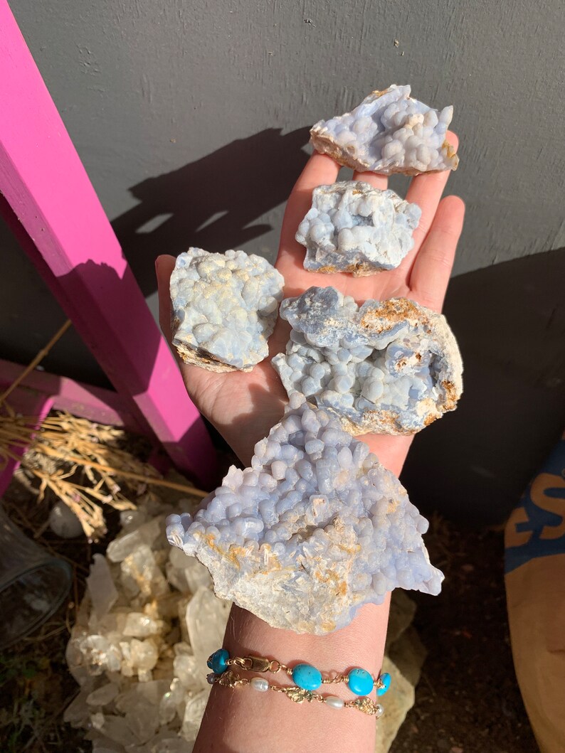 May include: Four blue and white agate crystal clusters with a rough, natural texture. The clusters are various sizes and shapes, with some having a more rounded form and others being more angular.