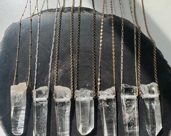 Puede incluir: Ocho collares con puntas de cristal y cadenas de diferentes estilos. Las cadenas son doradas, plateadas y negras. Las puntas de cristal son transparentes y facetadas.