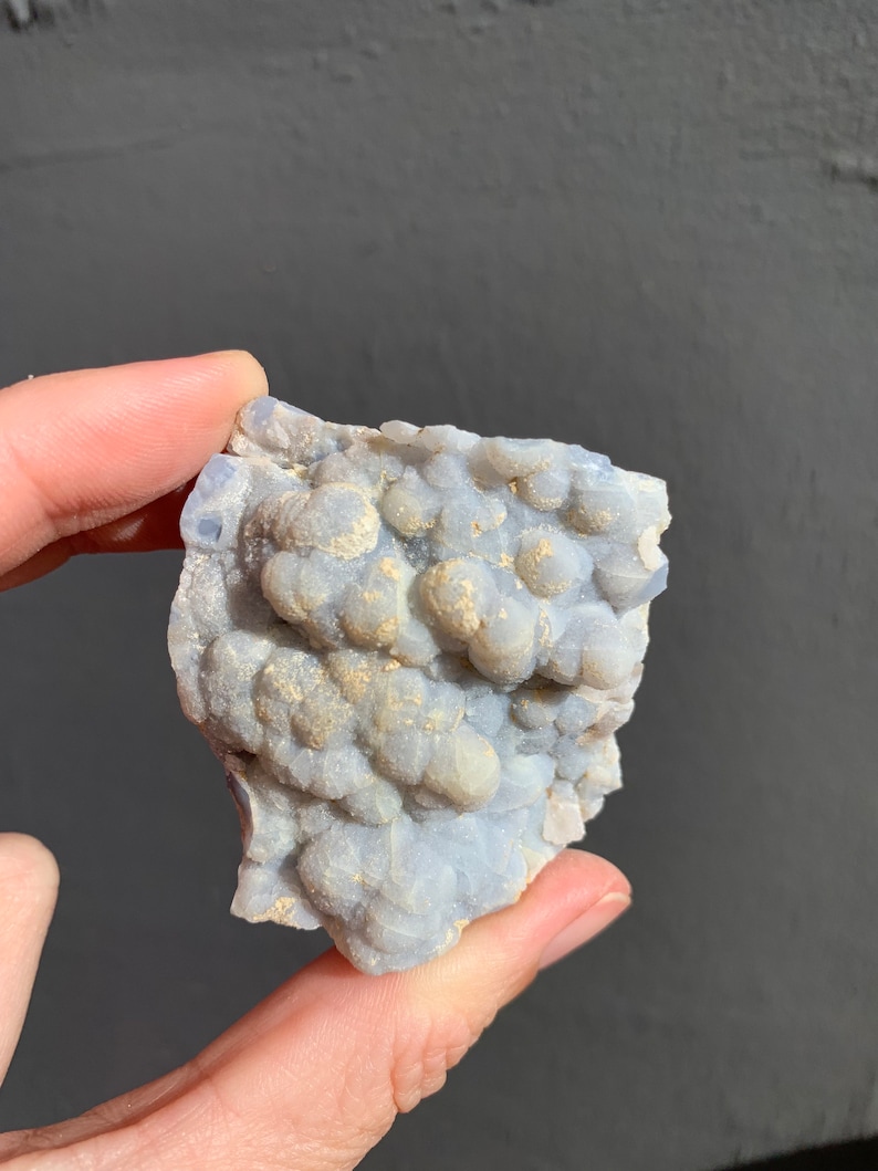 May include: A close-up of a light blue and white agate geode with a rough, textured surface. The geode is filled with small, round, white crystals.