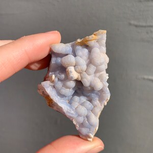 May include: A blue and white agate geode with a cluster of small, round nodules. The geode is rough and has a natural, organic shape.