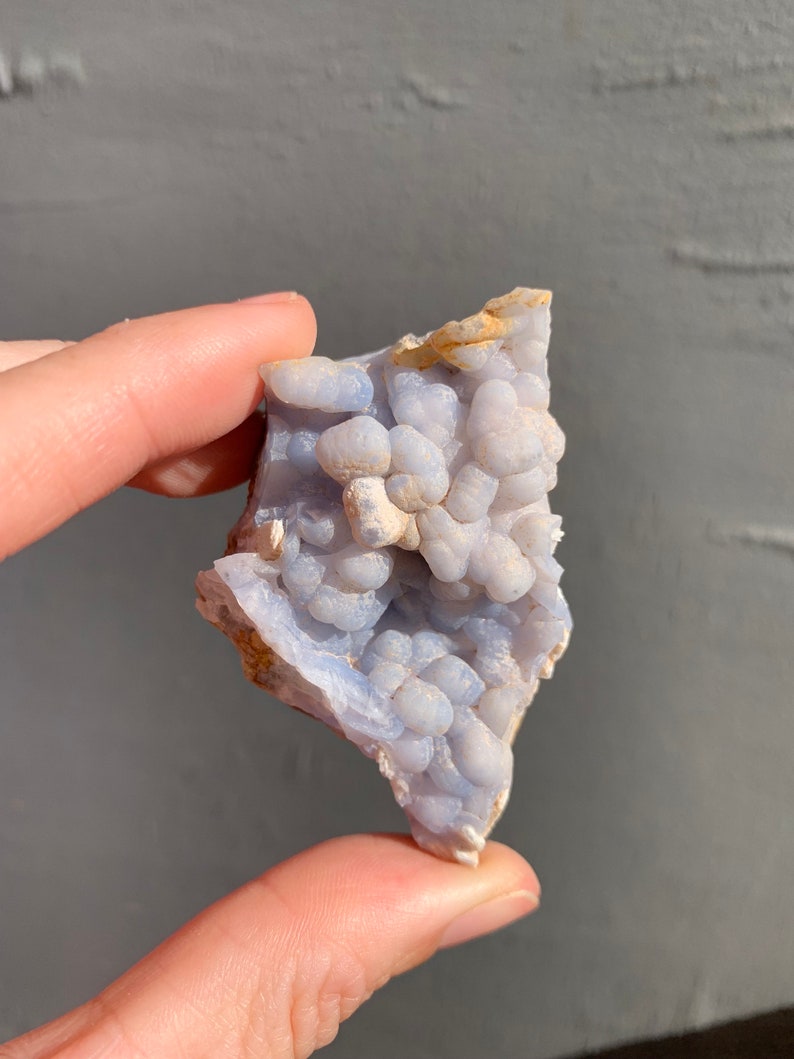 May include: A blue and white agate geode with a cluster of small, round nodules. The geode is rough and has a natural, organic shape.